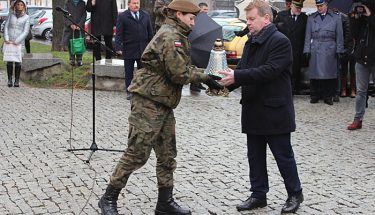 Zdjęcie z uroczystych obchodów Narodowego Dnia Pamięci Żołnierzy Wyklętych. Kurator oświaty podaje harcerce zapalony znicz, który zostanie postawiony przed Pomnikiem Ofiar Komunizmu