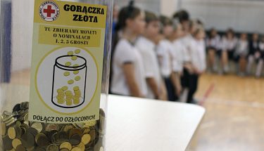 Zdjęcie z inauguracji dwudziestej edycji „Gorączki Złota”. Na pierwszym planie puszka wypełniona monetami, w tle stoją dzieci ubrane w stroje galowe