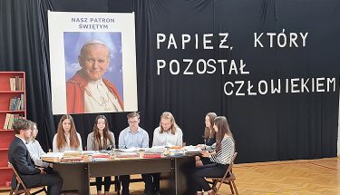 Zdjęcie przedstawia uczniów zgierskiej szkoły siedzących przy stole, w tle - obraz z Janem Pawłem II