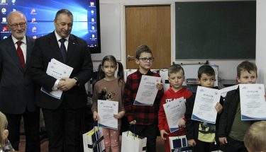 Na zdjęciu grupka dzieci z dyplomami i nagrodami, kurator oświaty i prezes pabianickiego oddziaółu PTTK