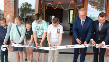 Zdjęcie przedstawiające uczniów i nauczycieli przecinających wstęgę przed siedzibą placówki edukacyjnej
